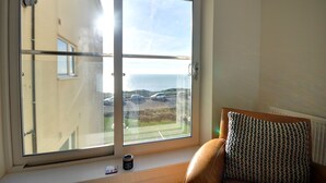 Una habitación con un gran ventanal corredero que da a un balcón con vistas a coches y un edificio.