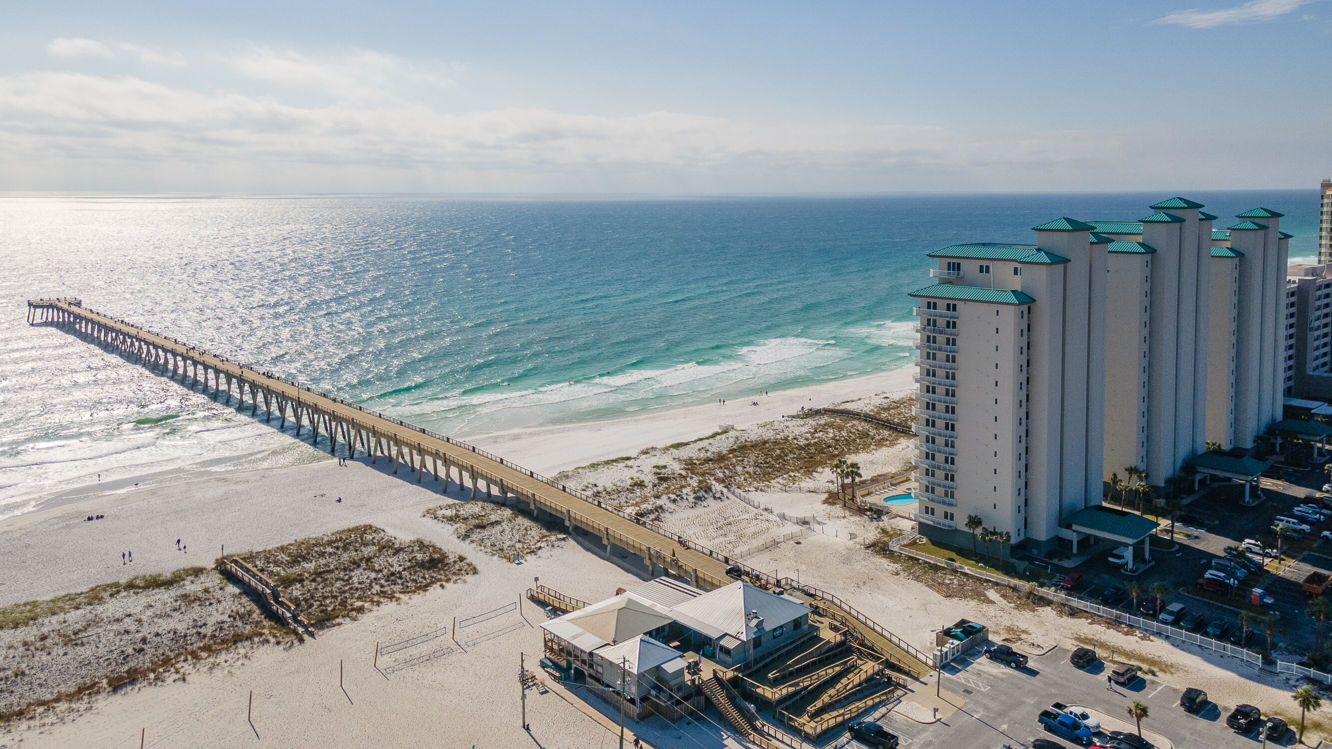A coastal hotel with a pier extending into the ocean, beachfront access, and high-rise buildings nearby.