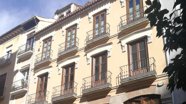 Un immeuble à plusieurs étages doté de balcons, de grandes portes en bois et d’un magasin situé au rez-de-chaussée où sont exposés divers articles.
