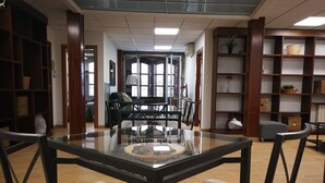 Une pièce spacieuse avec une table à plateau en verre, deux fauteuils rembourrés, un canapé et une bibliothèque.