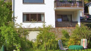 Une maison à deux étages avec un balcon, un mur en pierre et un jardin agrémenté de chaises et d’une table.