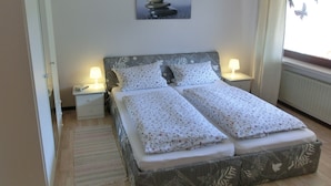 Un lit double avec une literie à motifs floraux, deux tables de chevet avec des lampes, un luminaire suspendu et un tableau au mur.