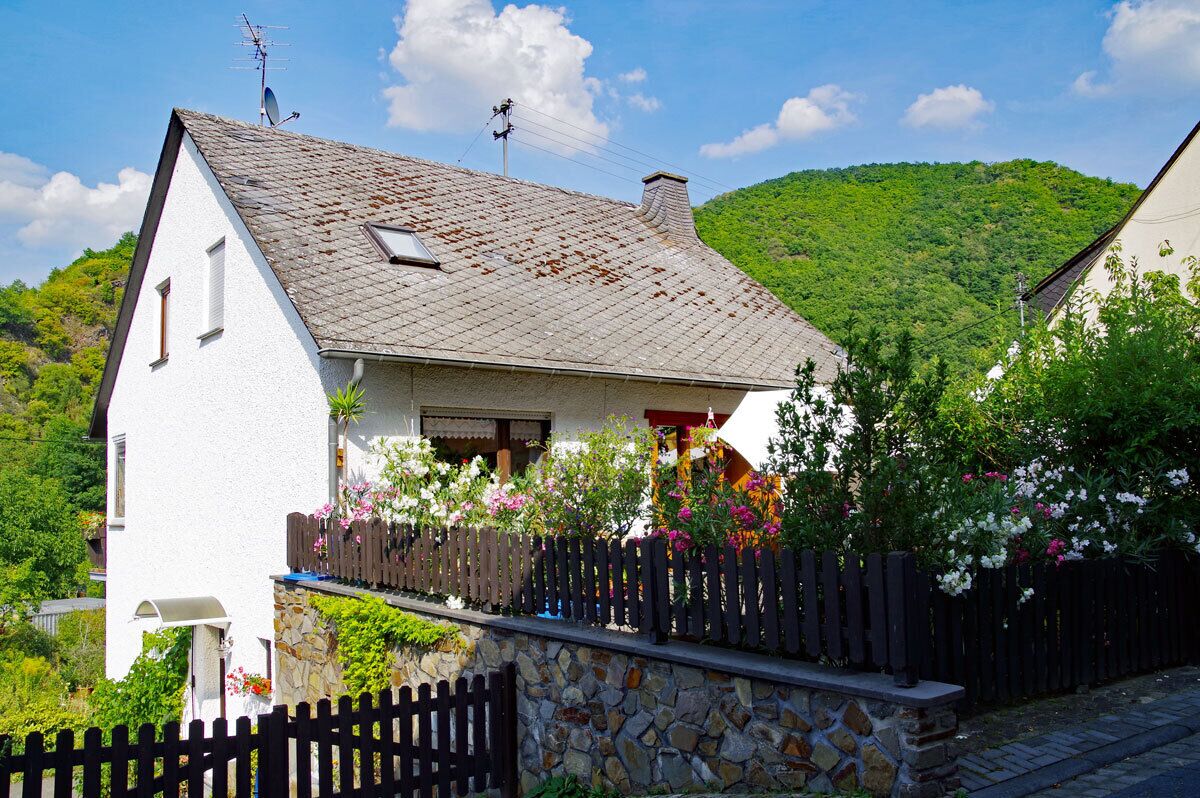 Ein weißes Haus mit Steinfundament, geneigtem Dach und Holzzaun.