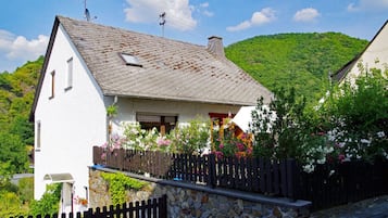 Ein weißes Haus mit Steinfundament, geneigtem Dach und Holzzaun.