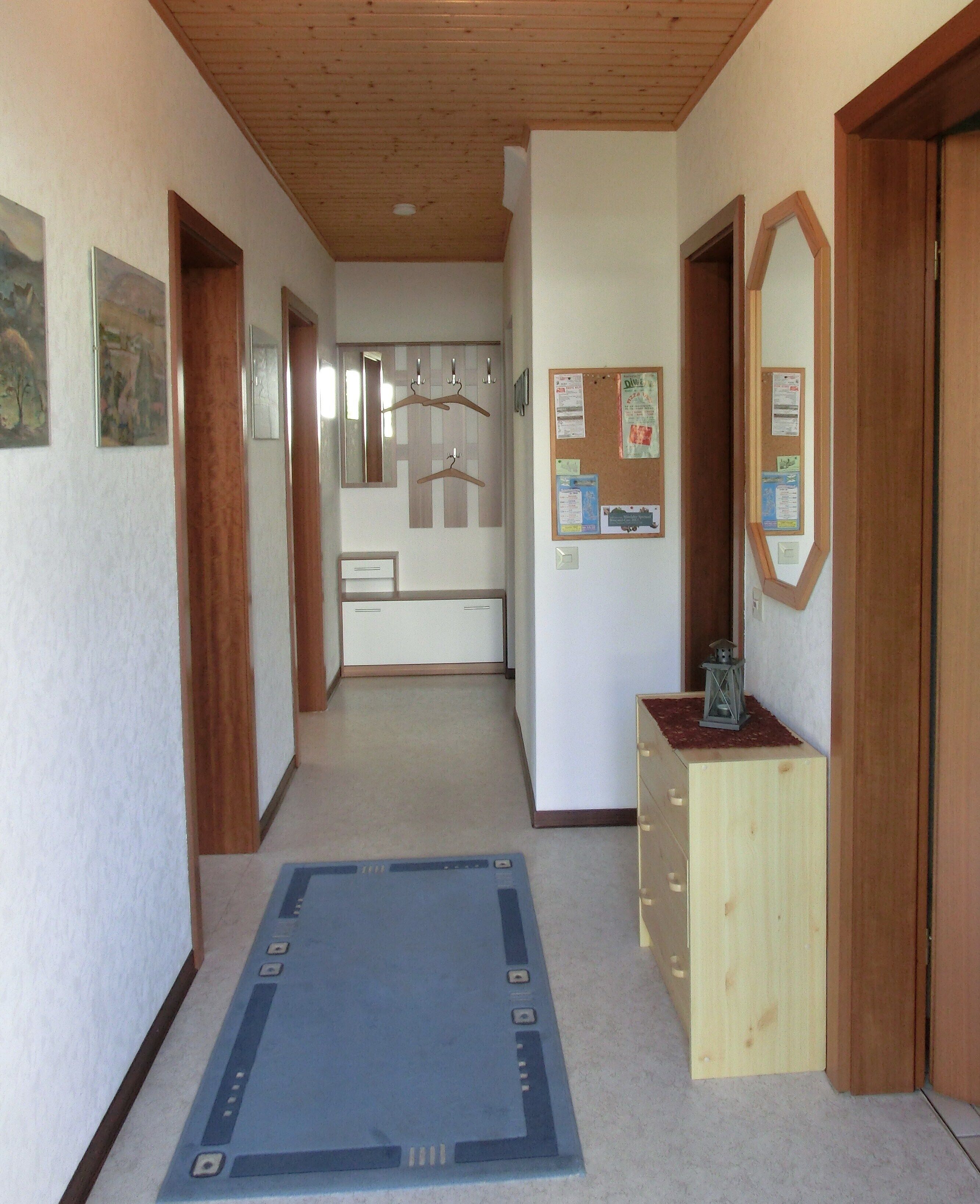 A hallway with wooden doors, a bulletin board, and a blue rug.