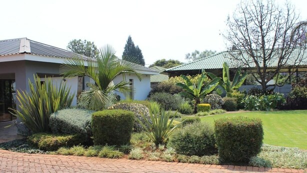 A house with a paved driveway, surrounded by well-maintained gardens and a lawn. - Sarum Lodge (Harare)