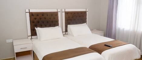 A double bed with a brown headboard, white bedding, and a remote control on the bed.