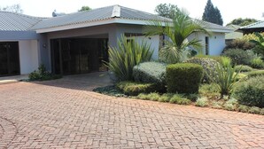 A modern house with a paved driveway, a covered entrance, and landscaped garden with various plants. - Sarum Lodge (Harare)
