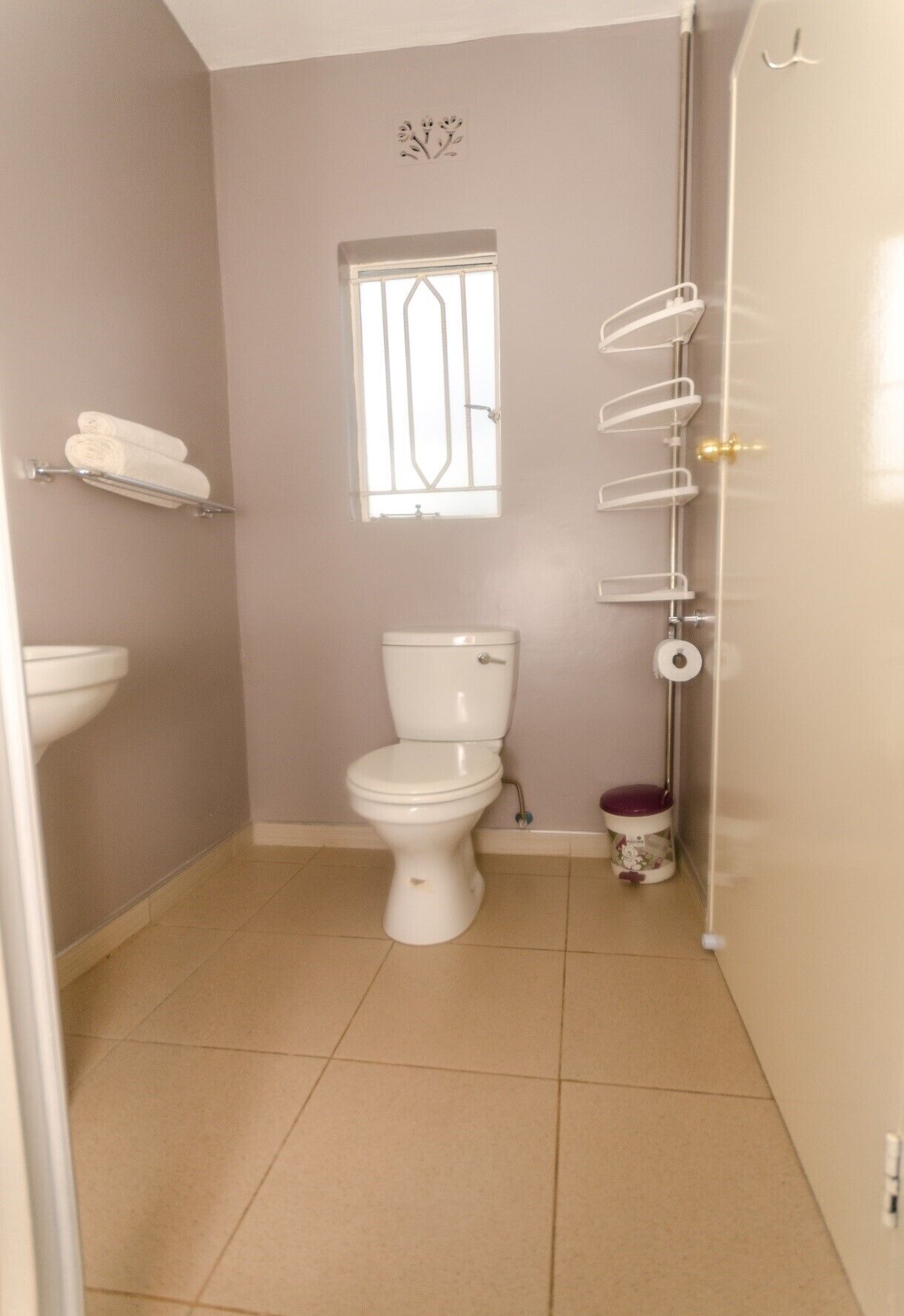 A small bathroom with a toilet, a window with bars, a towel rack, and a toilet paper holder.