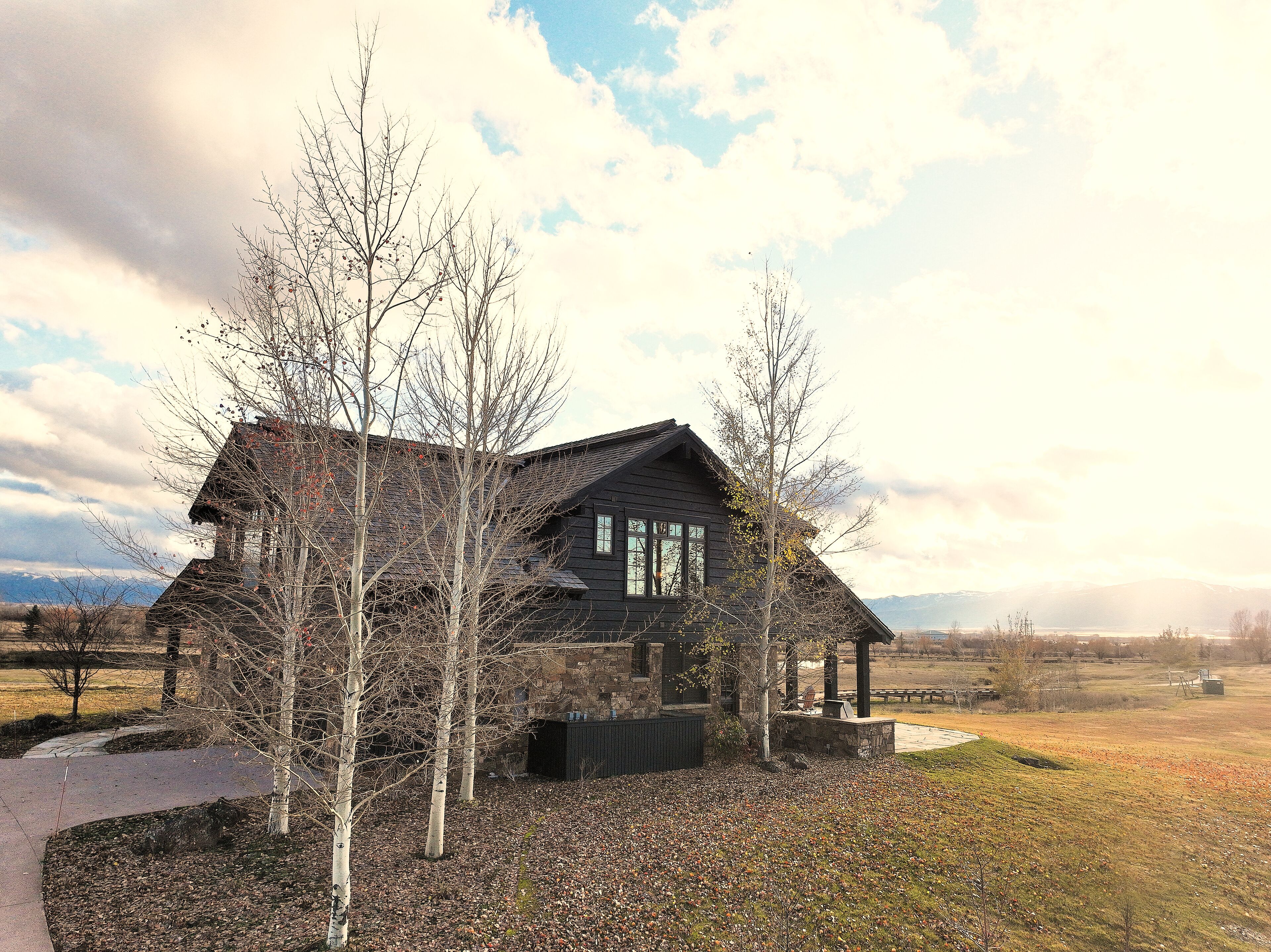 A two-story log cabin with a stone foundation, surrounded by leaf-covered ground and bare trees.