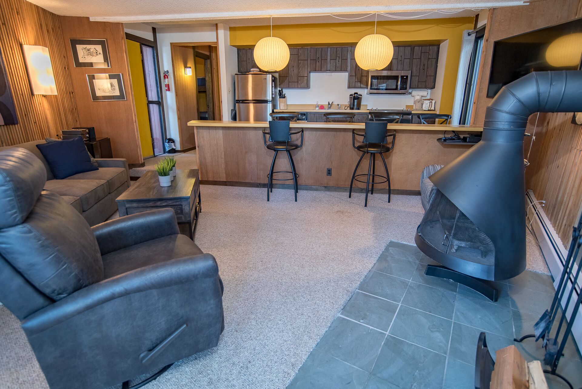 A modern living room with a sofa, a fireplace, and a kitchen area with bar stools.