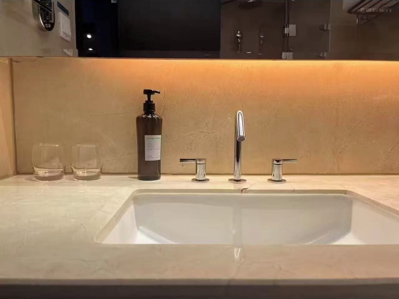 Un baño con un lavamanos grande, dos grifos y un dispensador de jabón.