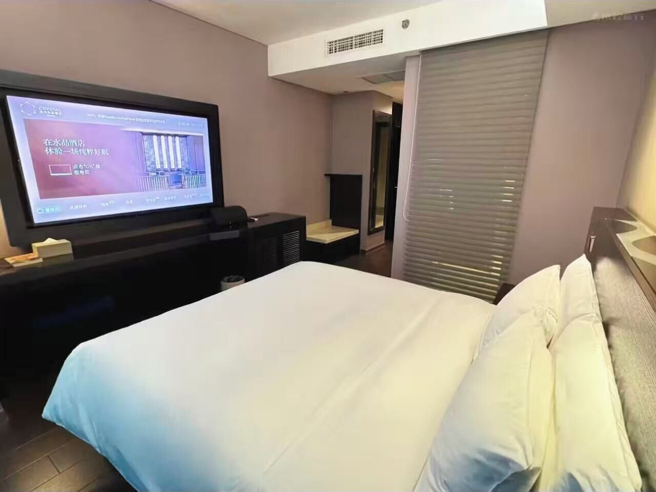 Una habitación de hotel con cama, televisión, escritorio y ventana con persianas.
