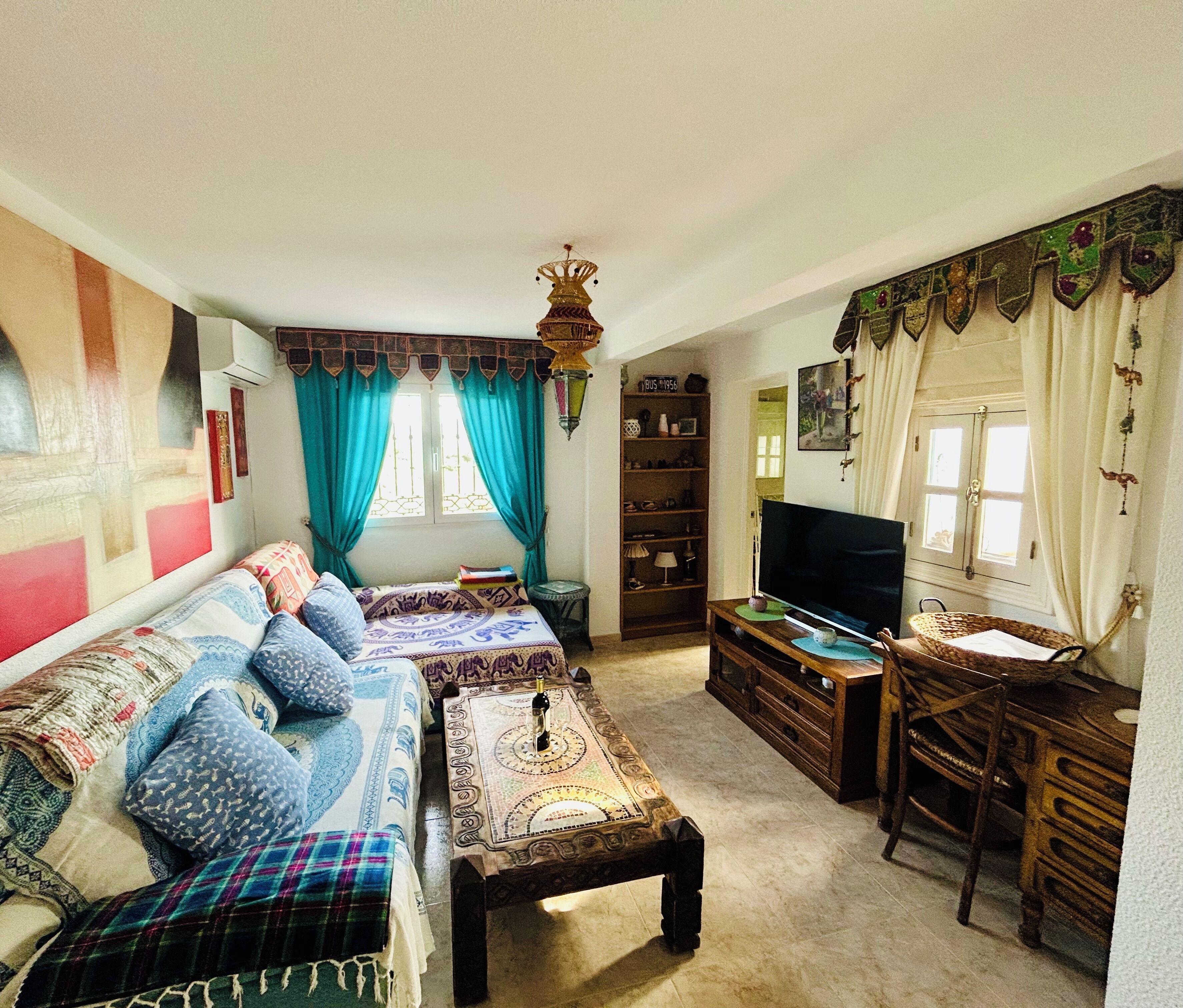 A cozy living room with a sofa set, a television, a wooden cabinet, and a window with curtains.