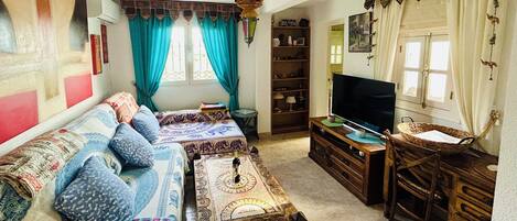 A cozy living room with a sofa set, a television, a wooden cabinet, and a window with curtains.