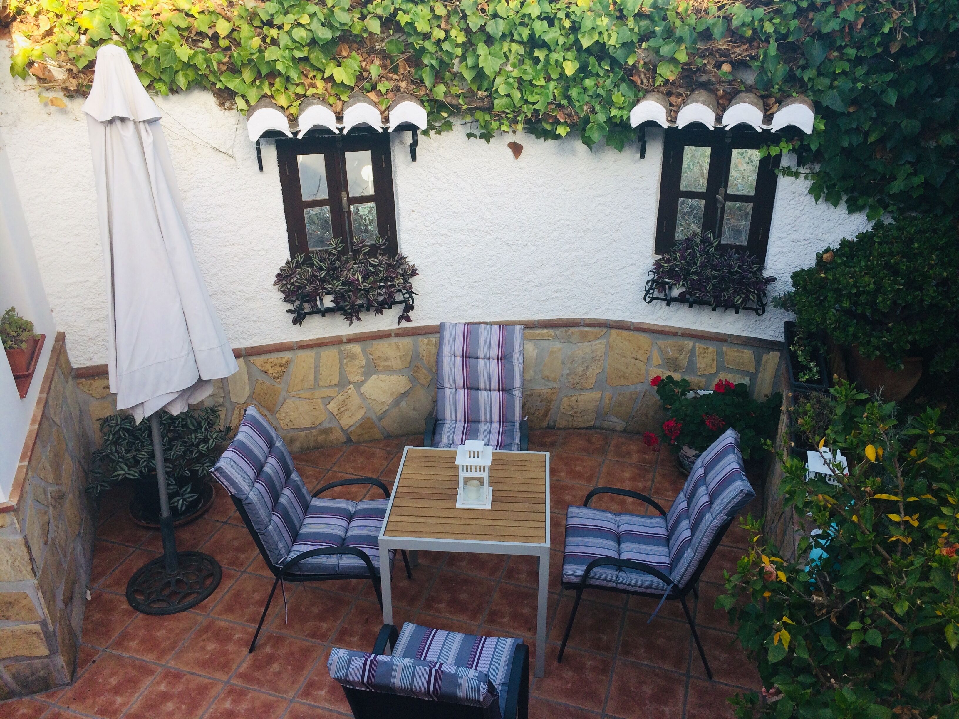 Eine Terrasse mit Tisch und Stühlen, umgeben von Steinmauern und viel Grün.