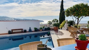 Mesa junto a la piscina con un plato de comida, un bol de fruta y una bebida.