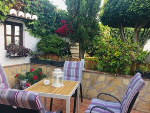 Eine Terrassengruppe im Freien mit Holztisch und gestreiften Stühlen, umgeben von Topfpflanzen und einer Steinmauer.
