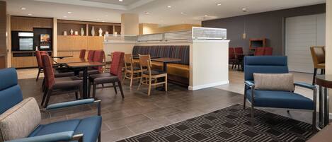 A modern hotel lobby with a dining area, seating arrangements, and a kitchen in the background.