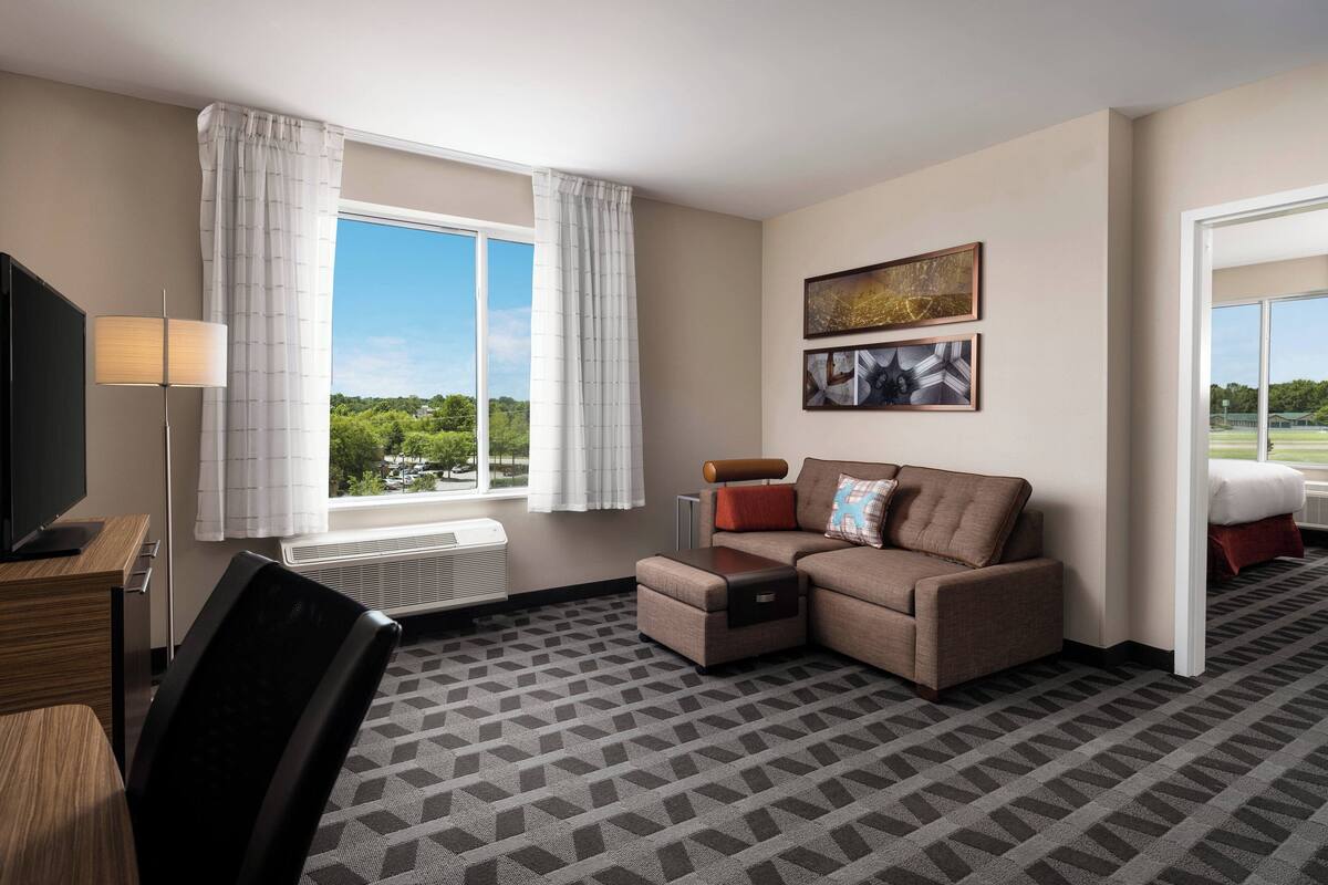 Une chambre d’hôtel avec un canapé, une télévision, un bureau et une fenêtre avec des rideaux.