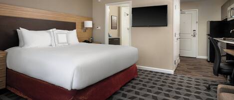 A hotel room with a large bed, a desk, a TV, and a bathroom visible through an open door.