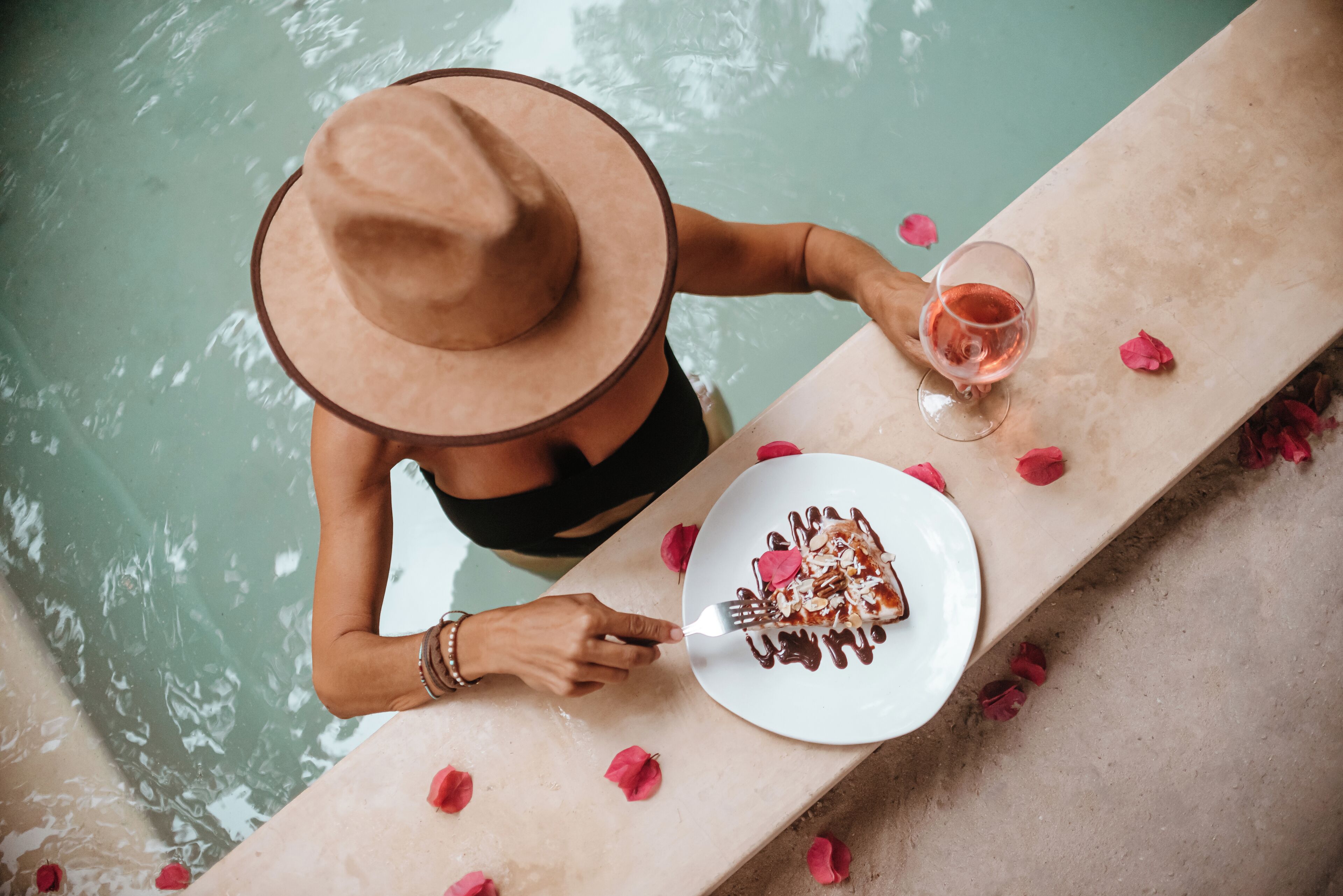 A person sitting by a poolside with a plate of food and a glass of drink.