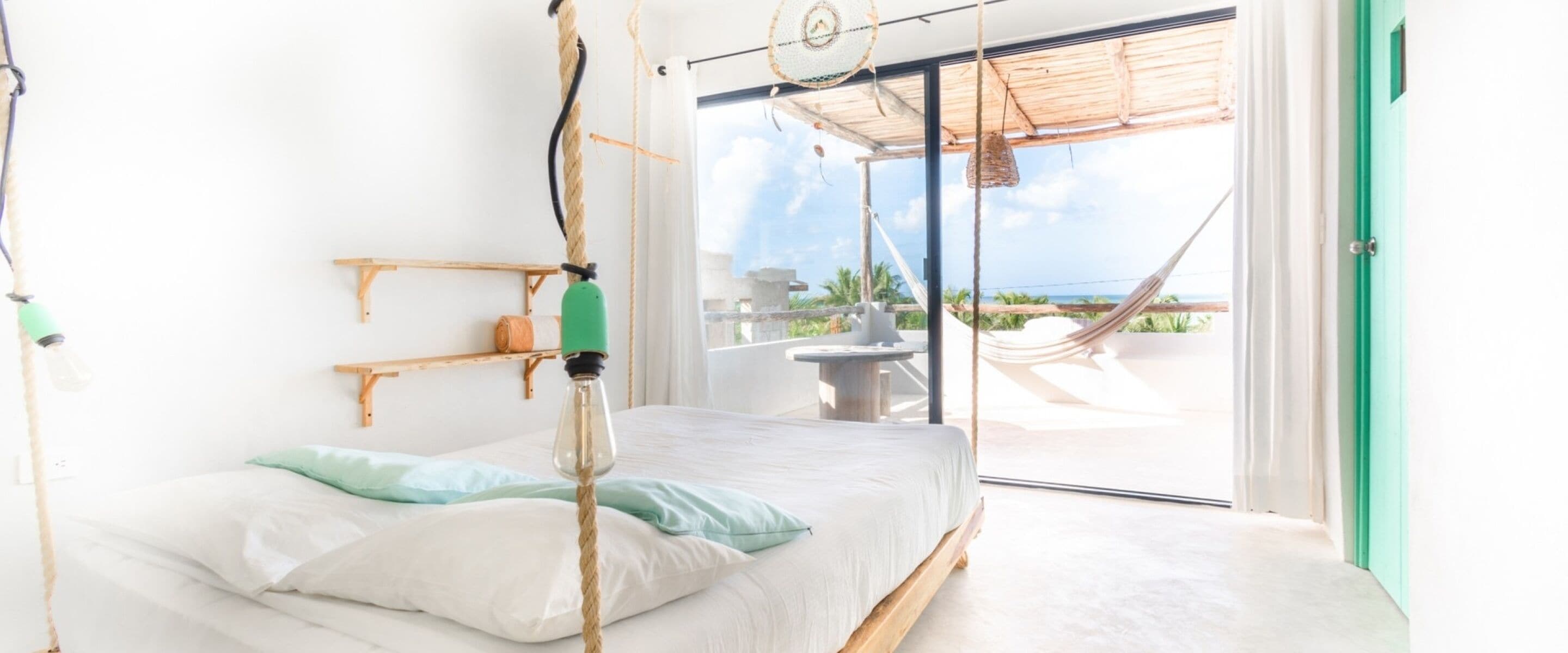 Ein heller Raum mit einem Bett, einer Hängematte draußen und Blick aufs Meer.
