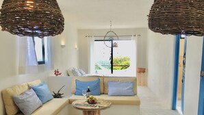 Una sala de estar moderna con un sofá, una mesita redonda con una botella y fruta, y un comedor con un mantel individual y cubiertos.