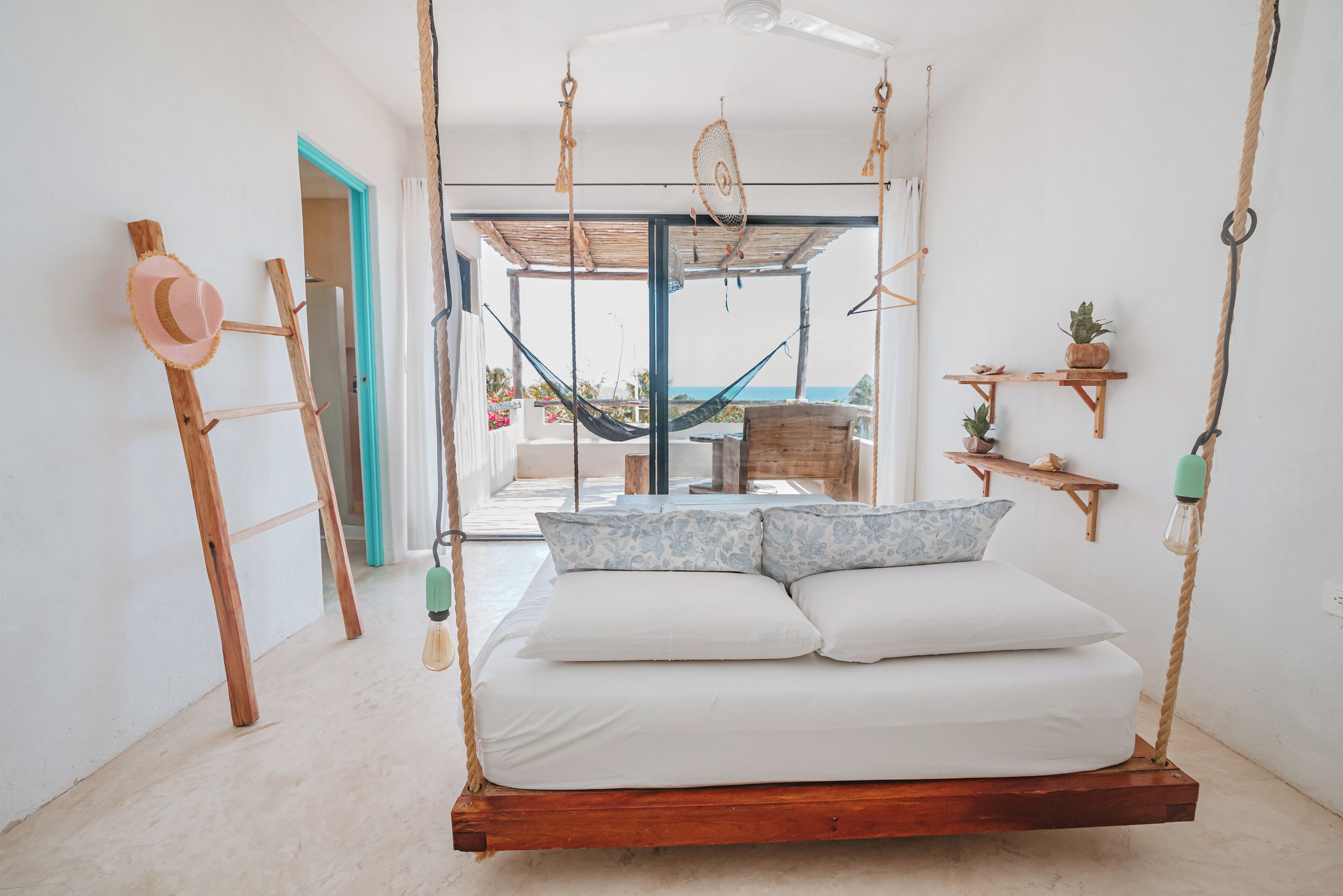 A bedroom with a hanging bed, a hammock, and a view of the sea.