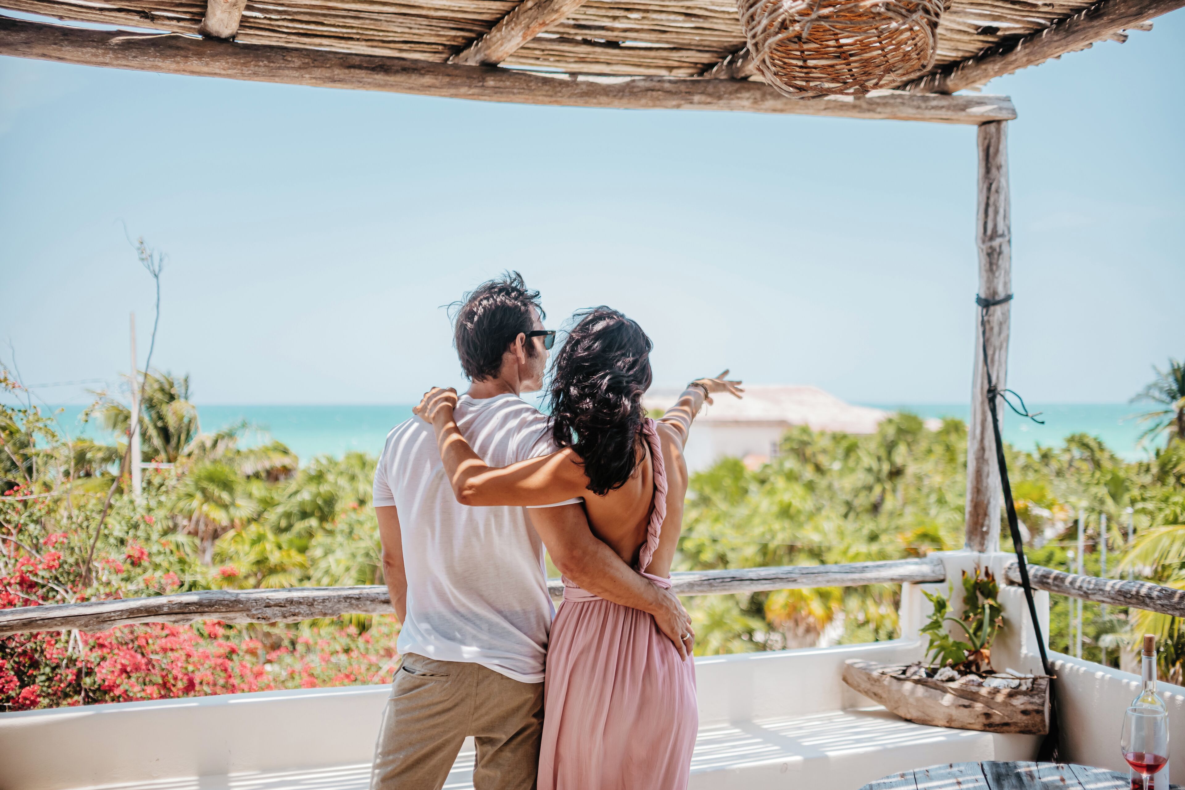 Un couple s’embrasse sur un balcon, avec vue sur l’océan et la végétation tropicale.