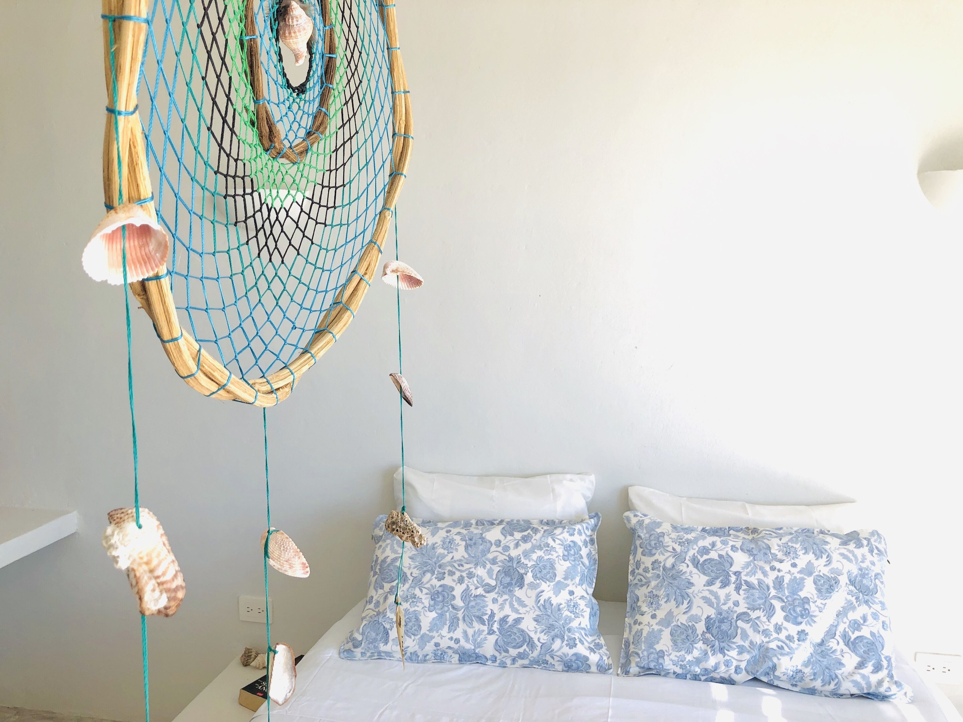 A bedroom with a bed, two pillows, a hanging dreamcatcher, and seashell decorations.