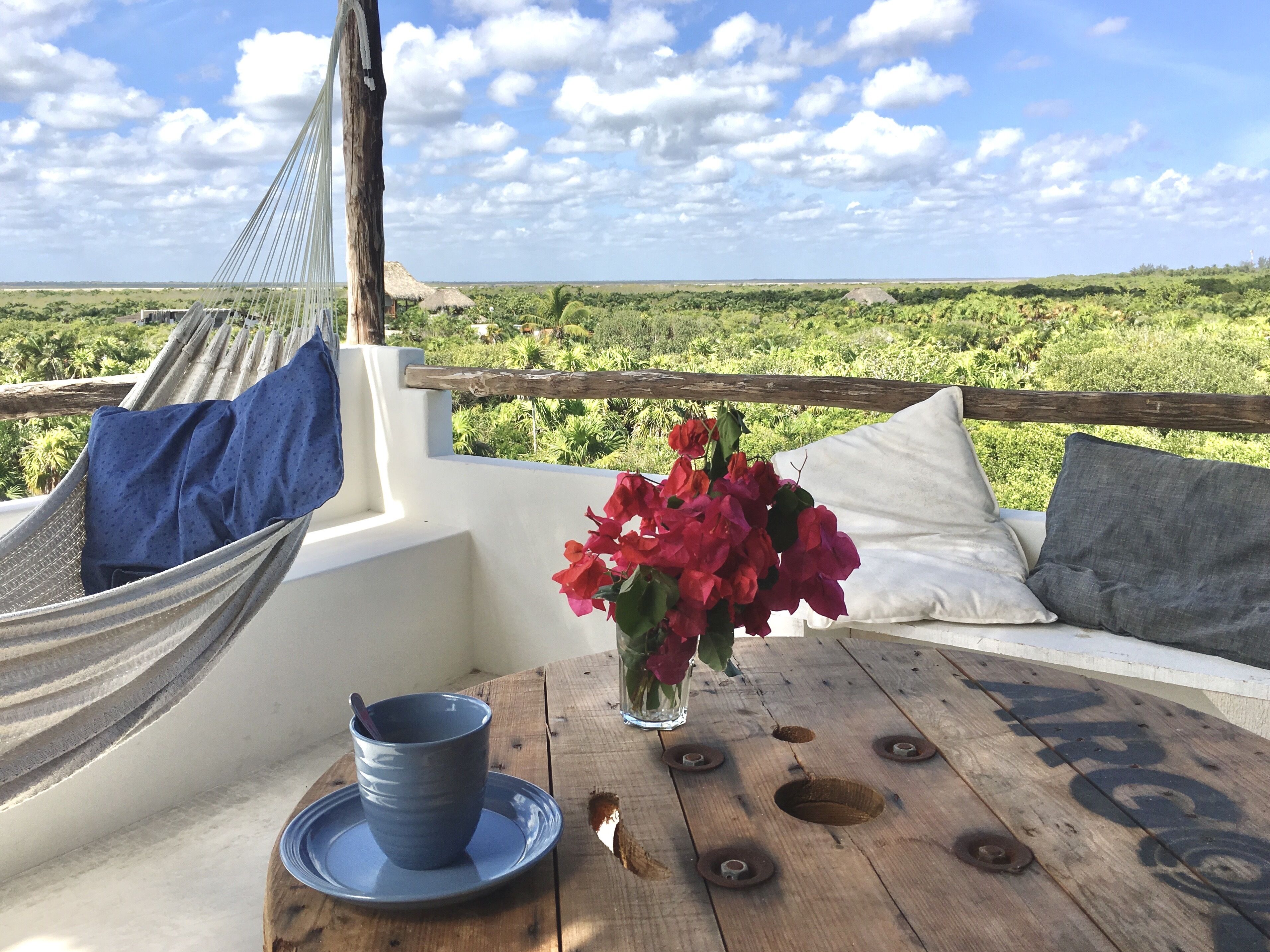 A hammock, a table with a cup and flowers, and a view of greenery.