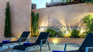 Eine Dachterrasse mit schwarzen Liegestühlen und blauen Kissen, umgeben von Pflanzen und einer Zierwand.
