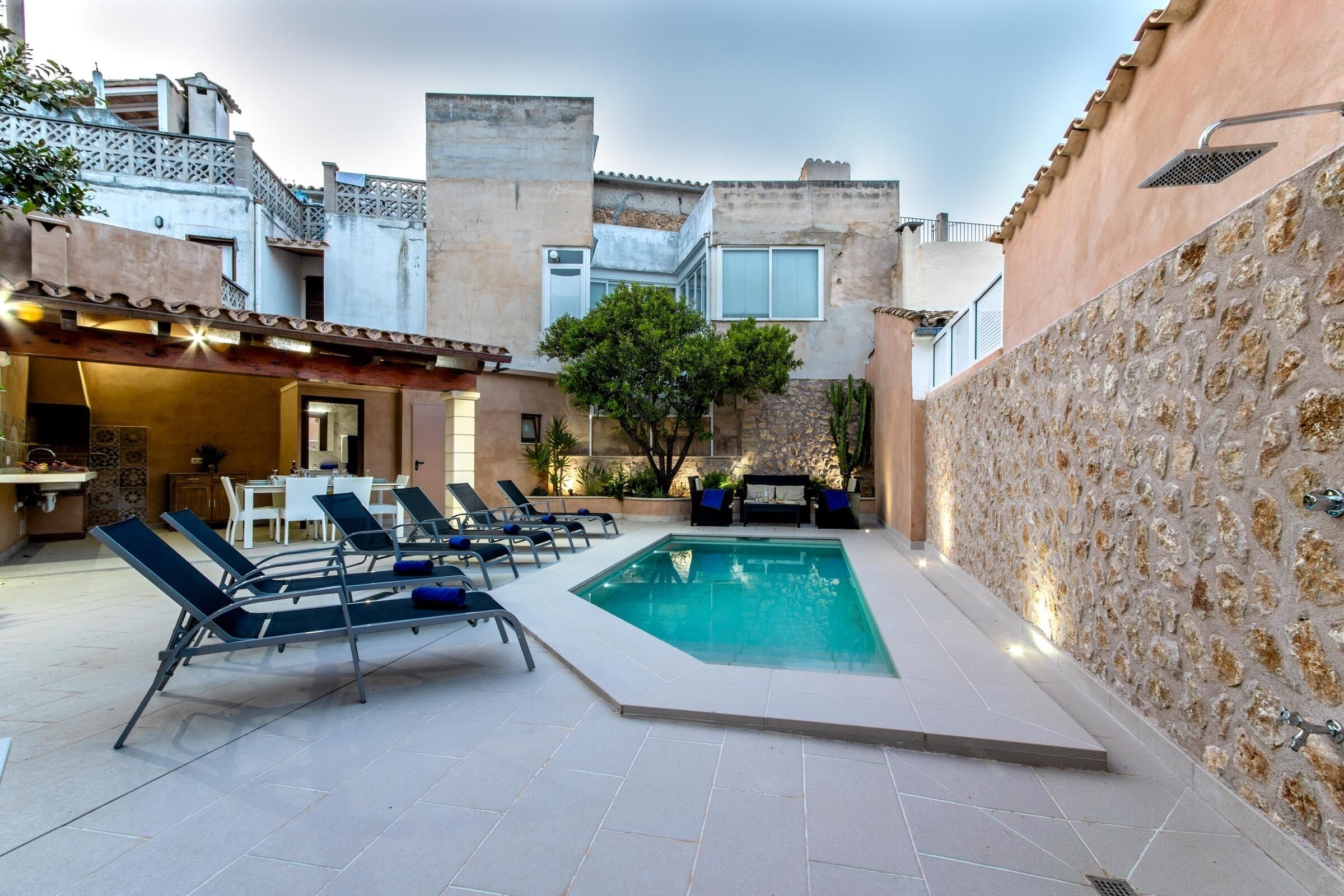 Una piscina con sillas de descanso, un comedor y una pared de piedra.
