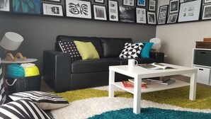 A modern living room with a black leather sofa, colorful pillows, a white coffee table, and a wall decorated with framed pictures.
