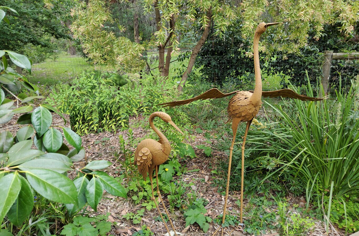 Un jardín con dos grandes esculturas de aves, rodeado de abundante vegetación y árboles.