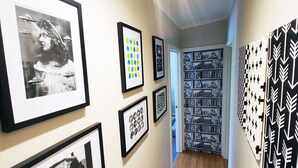 A hallway with framed artwork on the walls, a patterned rug, and a door leading to another room.