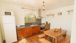Una cocina con armarios de madera, un refrigerador blanco, una mesa de comedor de madera con bancos, una ventana con vistas y una lámpara colgante.