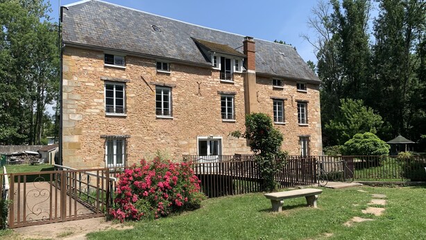 Un edificio de piedra con varias ventanas y un patio empedrado con un banco.