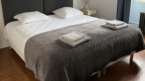 Una cama con una colcha gris, almohadas blancas y toallas dobladas.