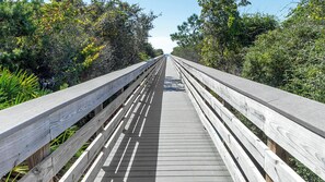 A wooden boardwalk with railings, surrounded by dense greenery and trees. - 3BR|2BA with Modern Décor, Pool & Tennis + Free Attraction Tickets! (Santa Rosa Beach)