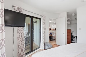 A modern bedroom with a TV, sliding glass door, and a view into a kitchen area.