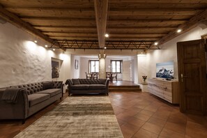 Een ruime woonkamer met een hoog houten plafond, een grote bank, een eethoek en een houten kast.