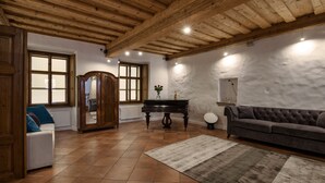 Een ruime woonkamer met een houten plafond, een vleugelpiano, een bank en een grote spiegel aan de muur.