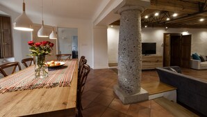 Een eetgedeelte met een houten tafel, stoelen, een vaas met bloemen en hangende hanglampen.