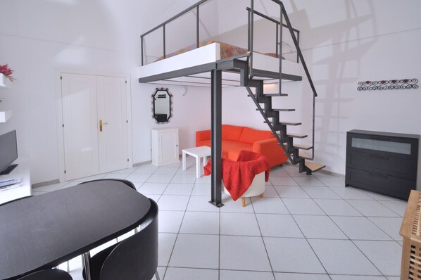 A room with a bunk bed, a sofa, a desk, and a television.