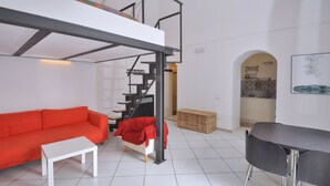 Ett modernt och kompakt bostadsutrymme med en våningssäng, en soffa, ett matbord och ett köksområde som syns genom en valvöppning.