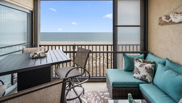 Ein Balkon mit Tisch und Stühlen, eine Couch mit Kissen und Blick auf den Ozean.