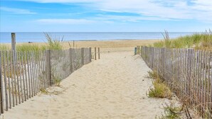 Ein sandiger Küstenweg führt zum Meer, gesäumt von Holzzaun.
