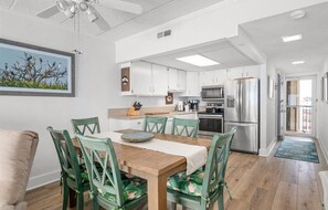 A modern kitchen with white cabinets, stainless steel appliances, and a dining area with a wooden table and green chairs.